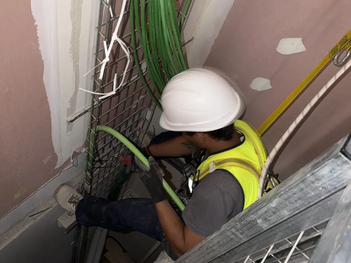 Electricista de Berpalux tendiendo líneas por el patinillo de verticales en la obra de C/ Orduña, Fuencarral